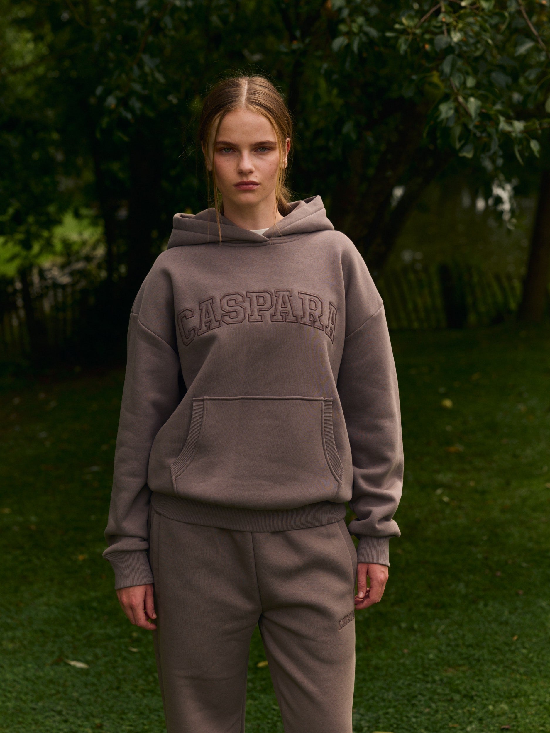 Woman wearing a walnut brown CASPARA hoodie and matching sweatpants outdoors.